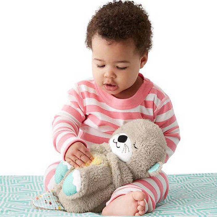 Fisher-Price Soothe 'n Snuggle Otter held by baby with white background
