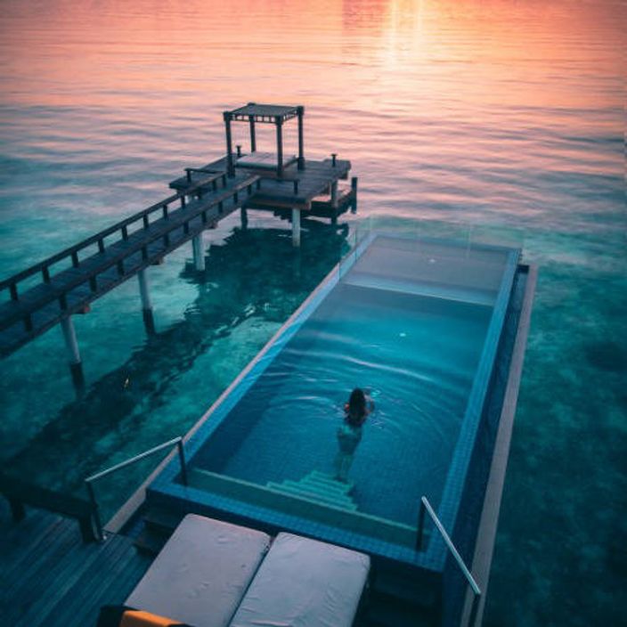 Woman in pool overlooking the ocean at sunset 