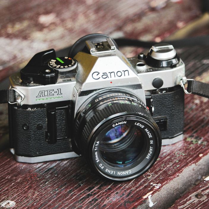 The Canon AE-1 camera sitting on a table with a roll of film and cups of coffee