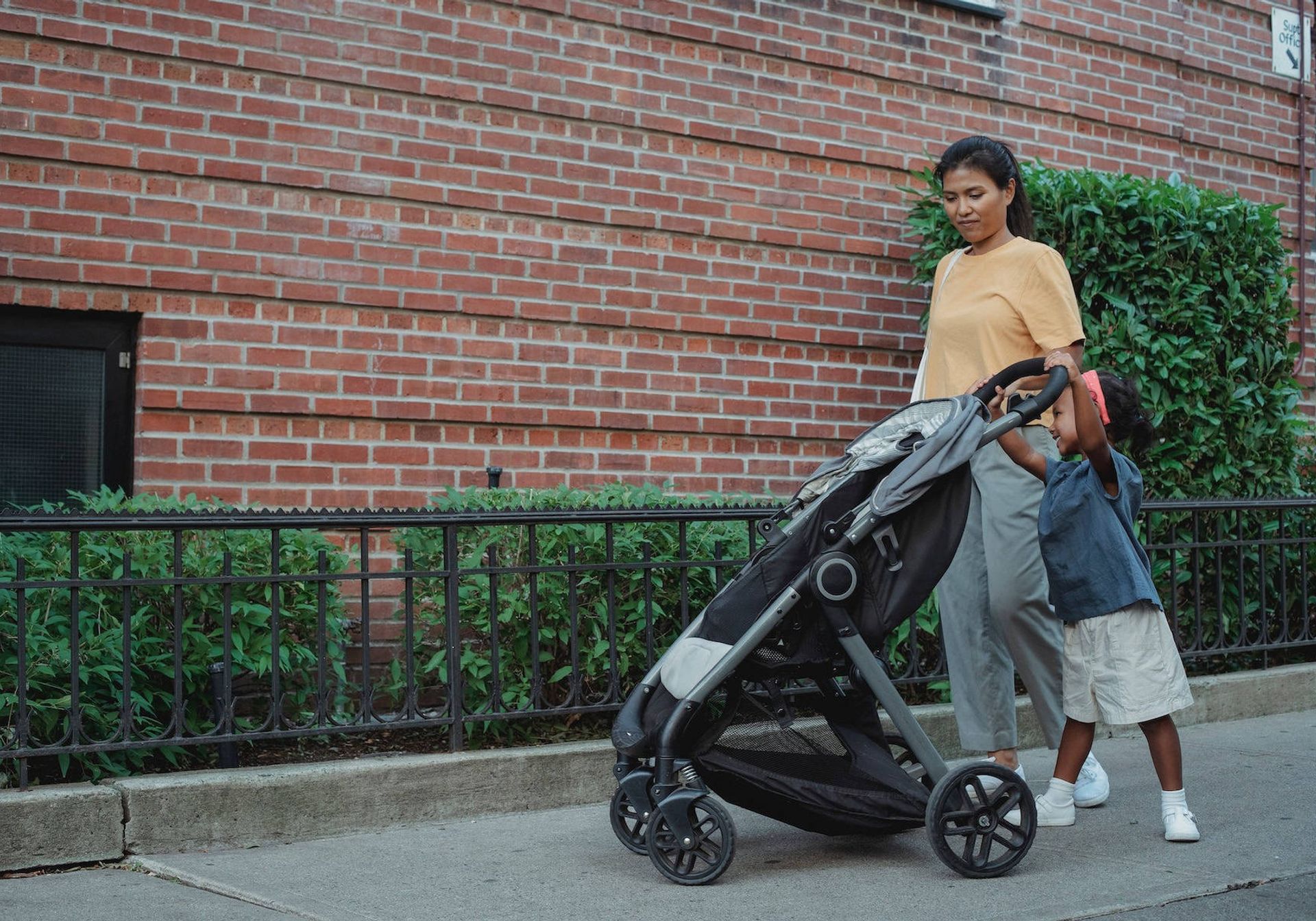 Mum walking with her daughter smiling and pushing the pram. 