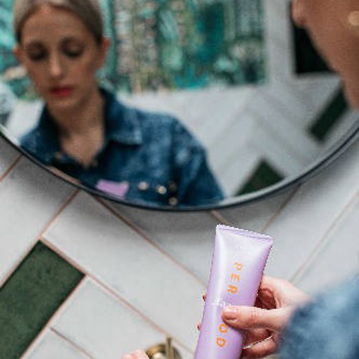 A girl holding a bottle of Period Faace masks in front of a mirror