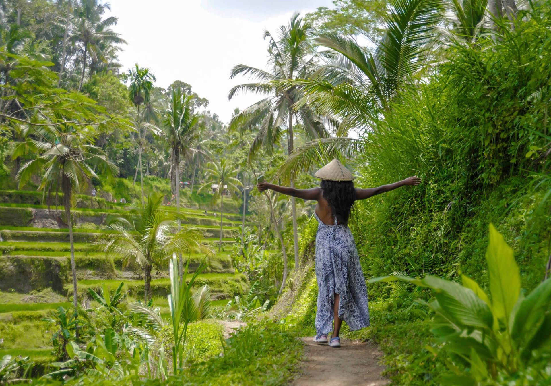 a black woman photographed from the back, with her arms spread in joy, overlooking a rice field