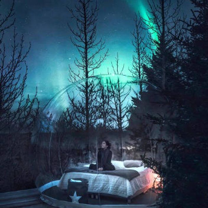 Woman in bubble dome under northern lights
