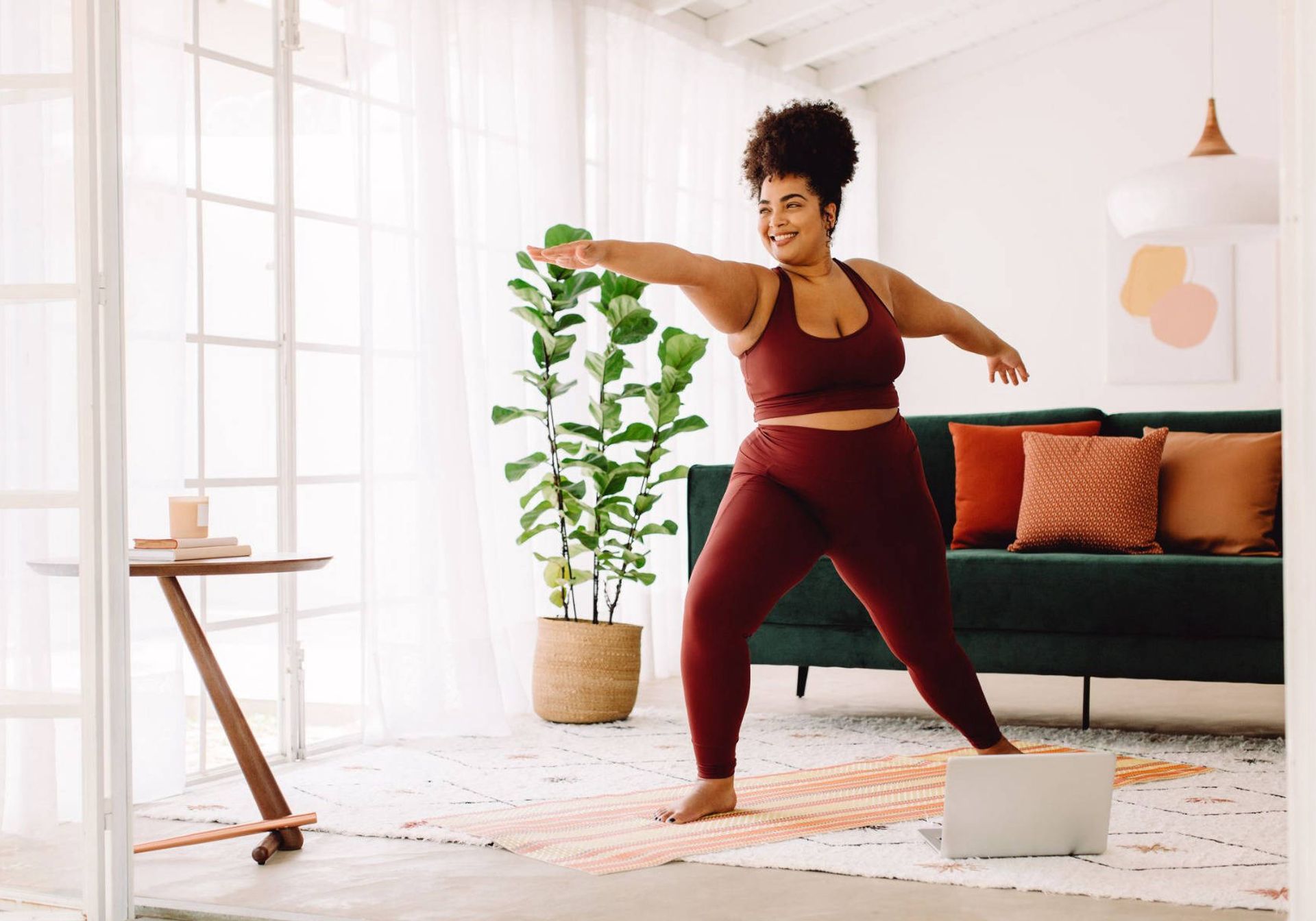 woman doing a yoga pose on a mat in her living room with a computer beside her