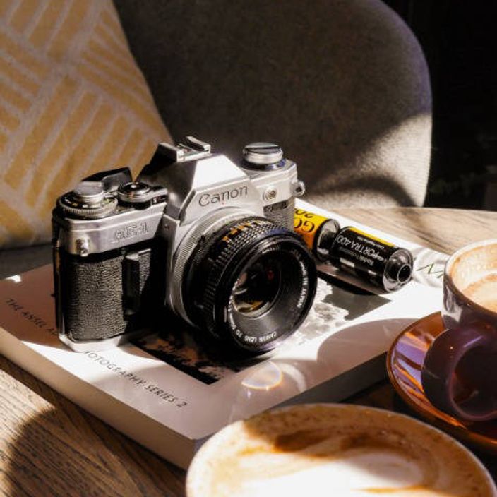 The Canon AE-1 camera sitting on a table with a roll of film and cups of coffee
