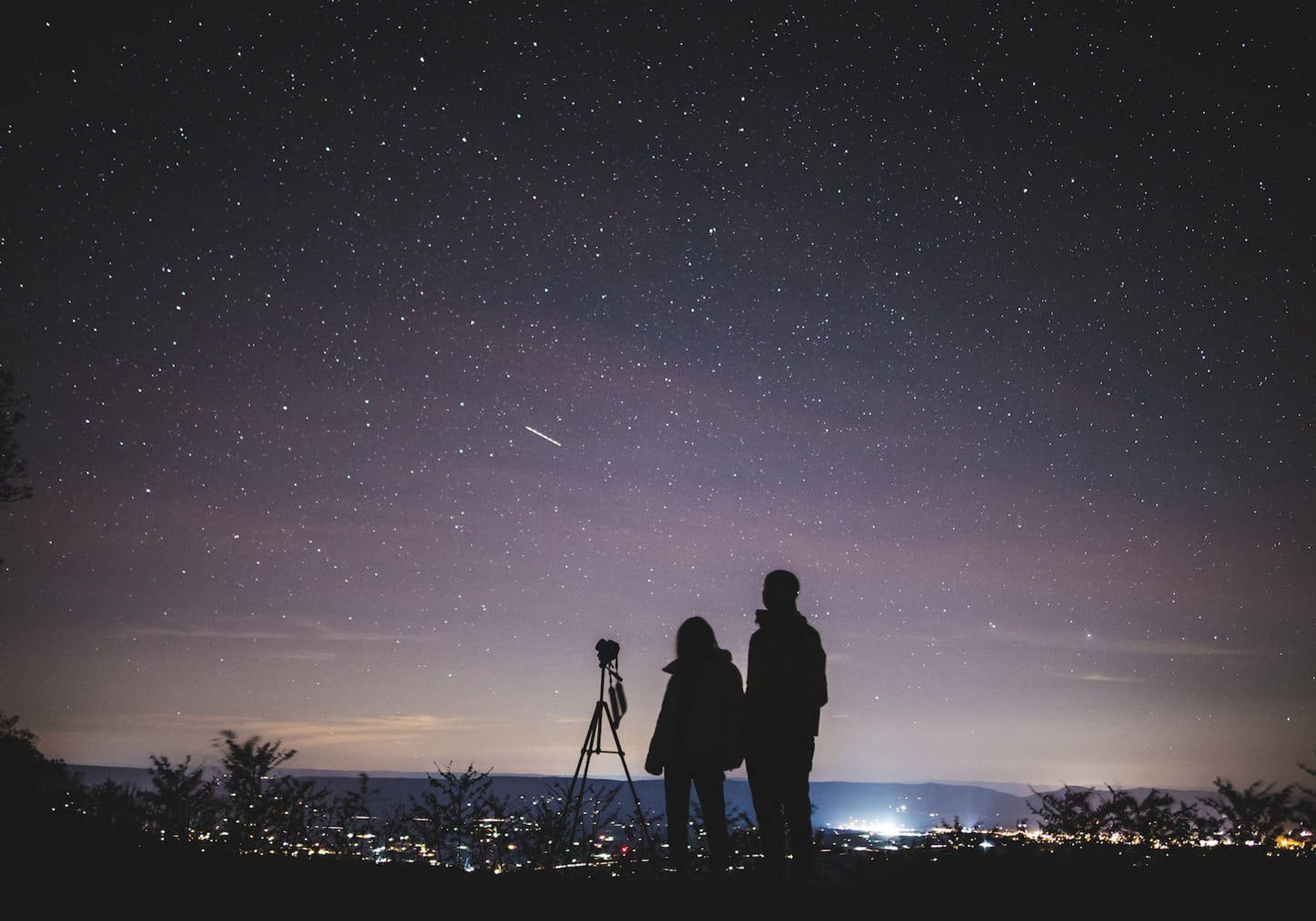 Two people stargazing on a hill