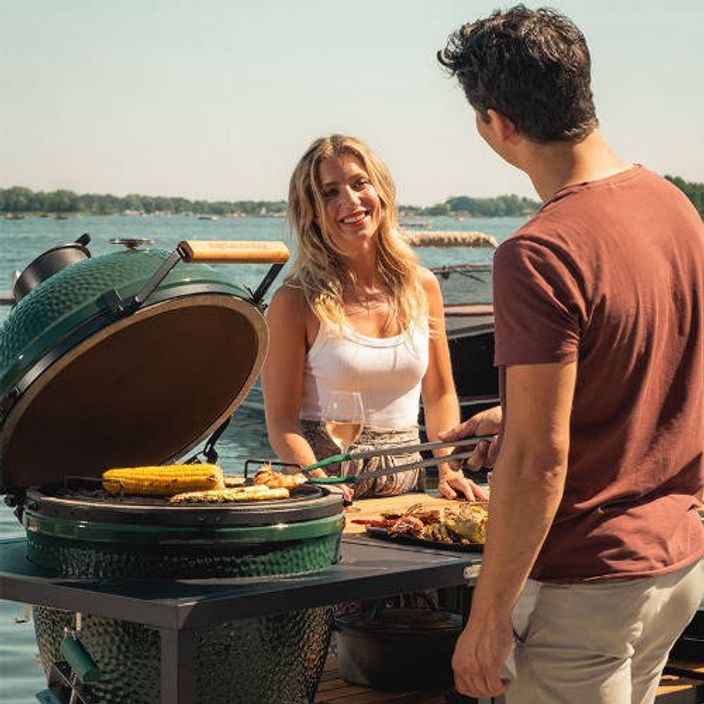 man looking at woman and grilling corn on a big green egg bbq