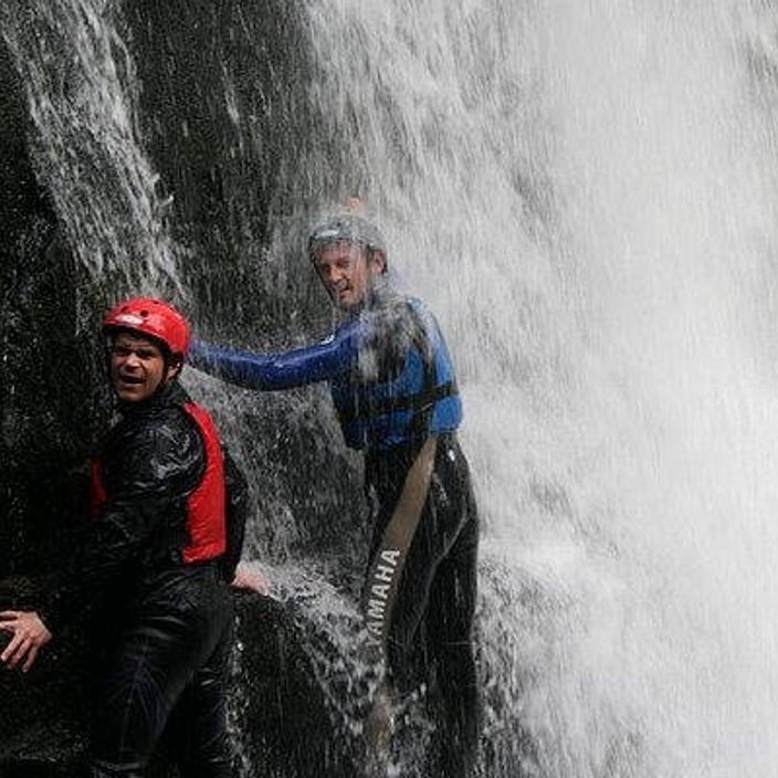 2 people walking through a waterfall in wales