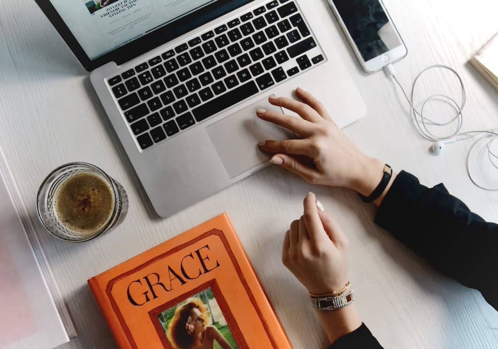 Person using a Macbook on a table next to a book