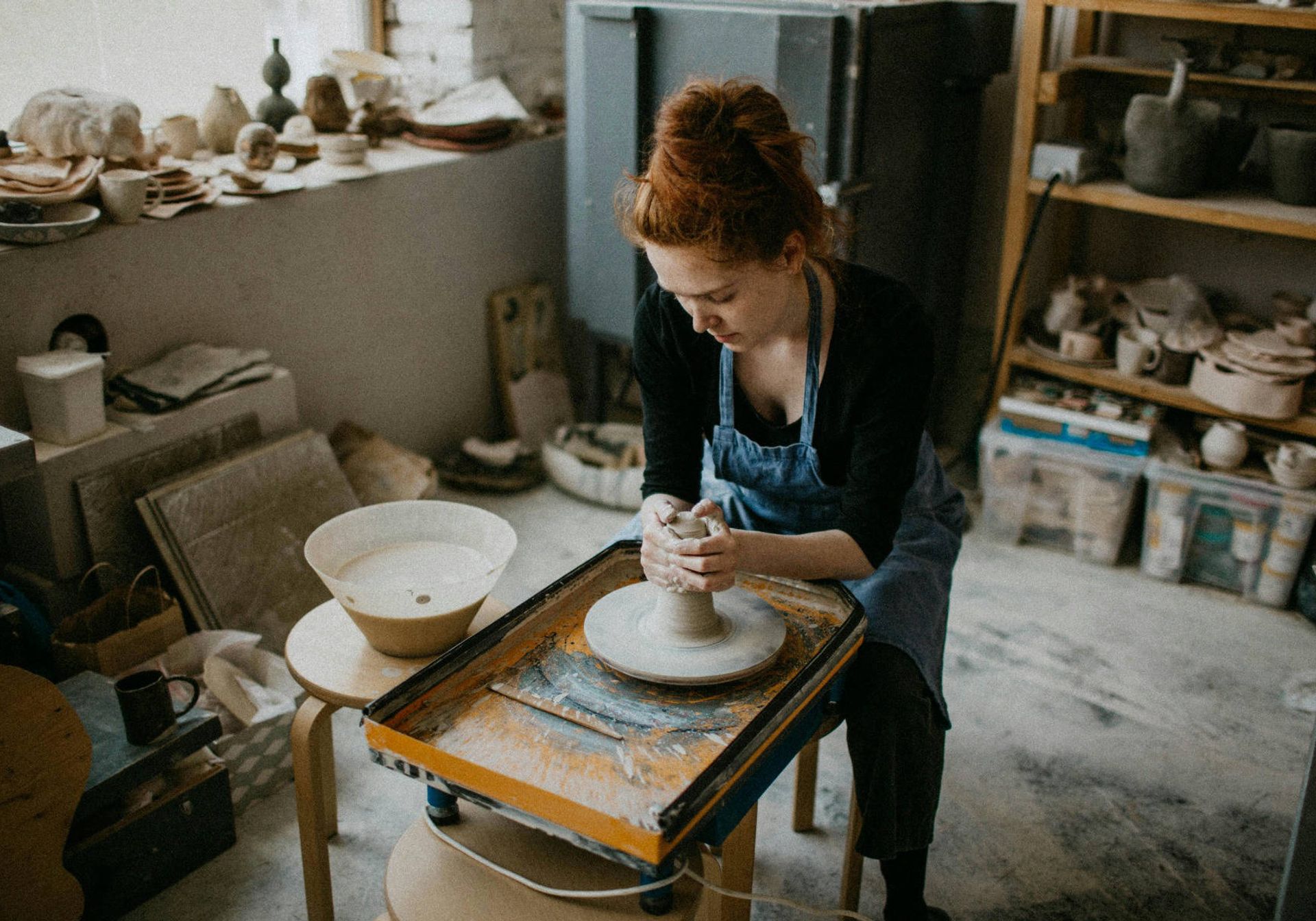 woman sitting at a throwing wheel shaping clay
