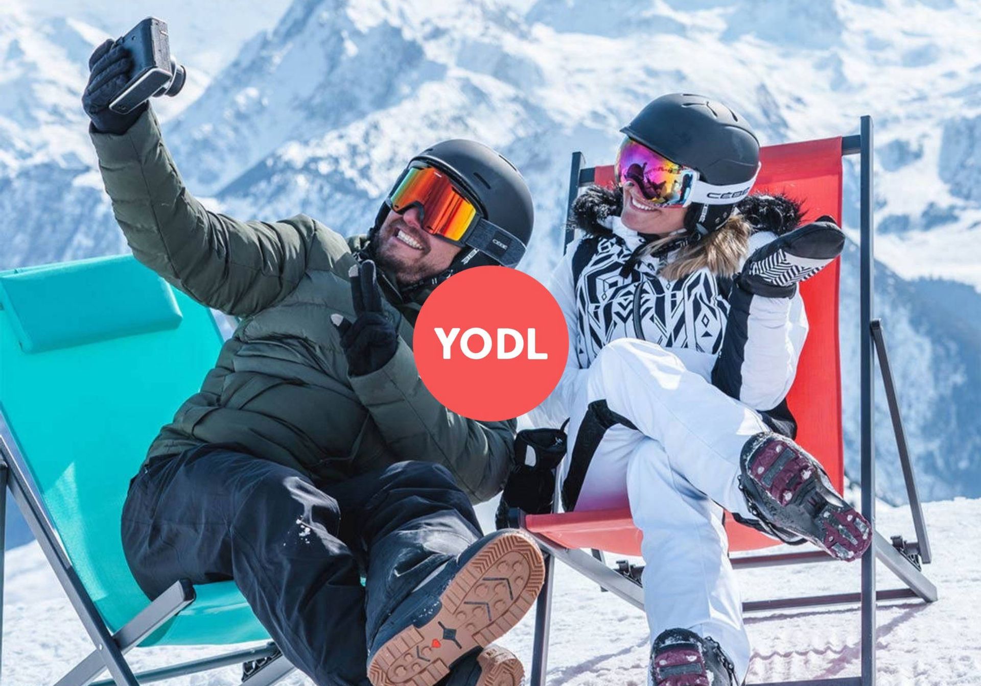 a white couple in skiing gear and sunglasses taking a selfie on two sun loungers on a skiing slope