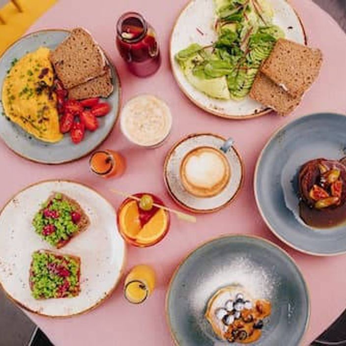 Avocado on toast, scrambled eggs and pancakes on a table with a pink cloth